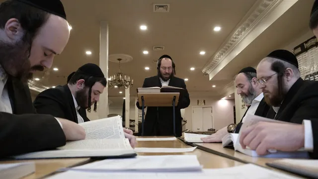 רבי משה אליעזר ליבערמאן שליט״א שטייט ביים שטענדער און זאגט דעם שיעור, ארום טיש זיצן די צוהערער און לערנען אין זייערע גמרות